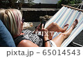 Senior woman looking on cell phone relaxing on a hammock in home garden, fuerteventura spain 65014543