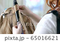 Close up of the hands of a professional hairdresser doing a curly hairstyle using a curling iron. The artist creates a curl hairstyle for long blonde hair in a beauty studio. 65016621