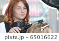 Beautiful red-haired master working with the hair of a client doing a curly hairstyle using a curling iron. The artist creates a curl hairstyle for long blonde hair in a beauty studio. 65016622