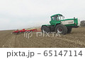Green tractor and red cultivator plows the ground on the field in the spring 65147114