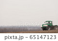 Green tractor and red cultivator plows the ground on the field 65147123