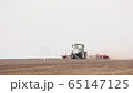 Green tractor and red cultivator plows the ground on the field in the spring 65147125