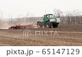 Green tractor and red cultivator plows the ground on the field in the summer 65147129