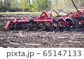 red cultivator plows the ground on the field in the summer 65147133