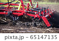 red cultivator plows the ground on the field 65147135