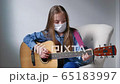 Portrait of a young girl wearing a mask playing guitar at home in quarantine time 65183997