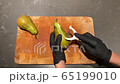 Woman in black kitchen gloves cleans pear peel with cutting knife 65199010