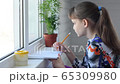Girl draws by the window with a pencil in an album 65309980