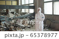 Portrait of young male scientist in protective suit standing in an abandoned factory amongst a big pileof rebel while looking into the camera during pandemic coronavirus quarantine time with big 65378977