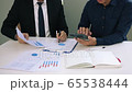 Managers and employees are calculating earnings on paper that contains graph data in the chart report and using calculators and collaboratively analyzing at the office. 65538444