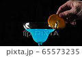 Blue cocktail. Hand puts a slice of orange on the edge of martini glass with blue summer cocktail on the table against black background. Concept of alcohol cocktail party, nightlife. Close up 65573235