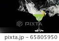 Green cocktail. White smoke or floating fog cloud in slow motion spreads down from the glass with green summer cocktail on the black table against black background. Concept of alcohol party. 4K 65805950