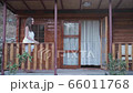 Smiling young woman stands on the porch and climbs on the railing sits and dangles legs. Long shot. Exterior of the modern wooden house. Woman in a towel leaves the house on the terrace 66011768