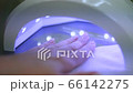Woman drying nails in ultraviolet light in home conditions. UV lamp gel polish manicure process close up. Female hand inside special machine fixing gel nail polish top view. Beauty salon procedure 66142275