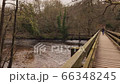 Young woman walking across wooden foot bridge in the woods over a river.  An attractive woman walking across a wooden footbridge over a river in the woods 66348245