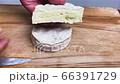 A young cheese maker cuts by not a big iron knife a piece of fresh soft cheese. Freshly cooked bio cheese, light white on the outside and creamy consistency on the inside. Puts the cut piece on anothe 66391729