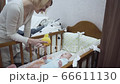 Young mother stands near the crib shows yellow toy to newborn baby. 66611130