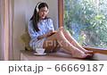 Cute asian woman reading book beside large window and drinking coffee in the morning. 66669187