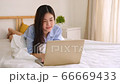Young asian woman working at home by computer laptop on bed and looking at camera with happily smile. 66669433