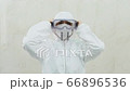 The doctor in a white protective suit with a hood puts on big plastic mask 66896536