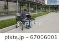 oung men who is sitting on a train station and working on his laptop 67006001