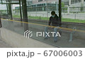young man who is waiting for a transportation in a glass bus stop or station and holding his phone 67006003