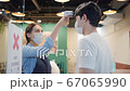 Asian restaurant staff using infrared thermometer on male customer's forehead before enter 67065990