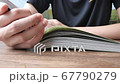 A young teenage boy is reading a comic book at home or library. Close up book on table and fingers hand of man student in black t-shirt sitting in a room with natural daylight from window, 4k.    67790279