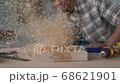 A young carpenter is cleaning a workbench from sawdust in a carpentry workshop. 68621901