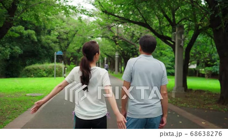 公園を手を繋いでウオーキングするシニアの夫婦の後ろ姿の動画素材
