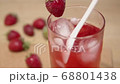 Putting cube of ice in strawberry cocktail on seaside and mixing it to make it colder. 68801438