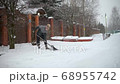 A young woman shovels snow in front of a private house on a winter evening 68955742