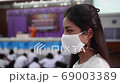 Asian female high school teacher and students on the semester start wearing a white mask, turn her face to look straight during the Coronavirus 2019 (Covid-19) epidemic. 69003389