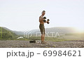Handsome strong muscular young guy with naked torso doing outdoors workout with dumbbells and tire from wheel on the hill on the wonderful nature background at daybreak 69984621