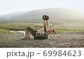 Handsome confident strong young man with tatoo lying on the tire from wheel and doing exercises with dumbells on the top of the hill surrounded picturesque nature in the summer morning 69984623