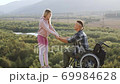Portrait of good-looking smiling happy couple where disabled man getting up from wheelchair with his wife's help and doing his first steps after desease or accident on the hill on the picturesque 69984628