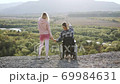 Good-natured happy satisfied woman and man in wheelchair holding their hands on the mount and watching at the unique landscapes around,view from back 69984631