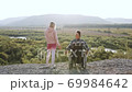 Back view of attractive relaxed handicapped man in wheelchair and his sporty wife which standing on the top of the hill and holding their hands watching at beautiful nature around 69984642