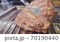 Piece of raw meat is turns with tongs on the grill net. Cooking unhealthy food. 70190440