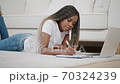 Millennial african ethnic woman student using laptop leaning at home, mixed race disciple distance education typing on notebook lying on the floor 70324239