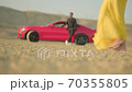 the girl walks on the sand in the desert,there is a red car behind 70355805