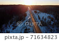 Aerial flight over the winter forest, top view and road under sunlight at sunset 71634823