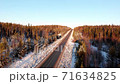 Aerial flight over the winter forest, top view and road under sunlight at sunset 71634825