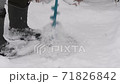 Drilling ice with an ice drill. Drilling holes in ice. Preparation before winter fishing. Legs in boots while drilling ice. Slow motion. 71826842