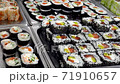 Young man choosing sushi rolls by hand and take it to the plate closeup. HD. Traditional meal sushi rolls big row of variety to the choice in the supermarket. 71910657