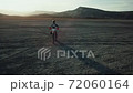 Drone view of man on motorbike rides on a dry lake with dust and beautiful hills on background in sunset 72060164
