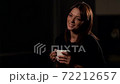 Portrait of a brunette woman with natural beauty. He is in the Studio on a dark background and drinks from a white Cup and smiles. 72212657
