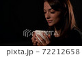 Portrait of a brunette woman with natural beauty. Is in the Studio room on a black background and drinks from a white Cup and enjoys. 72212658