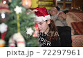 Young girl at home decorating Christmas Tree wearing Santa Hat with grandpa on the background 72297961
