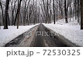 wet road between a snow covered woods 72530325